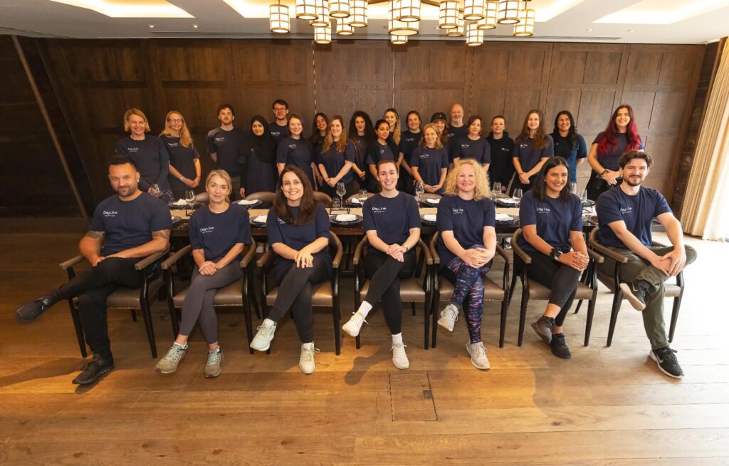 The Day One team at a dining table, with some members seated in front of the table and some standing behind it